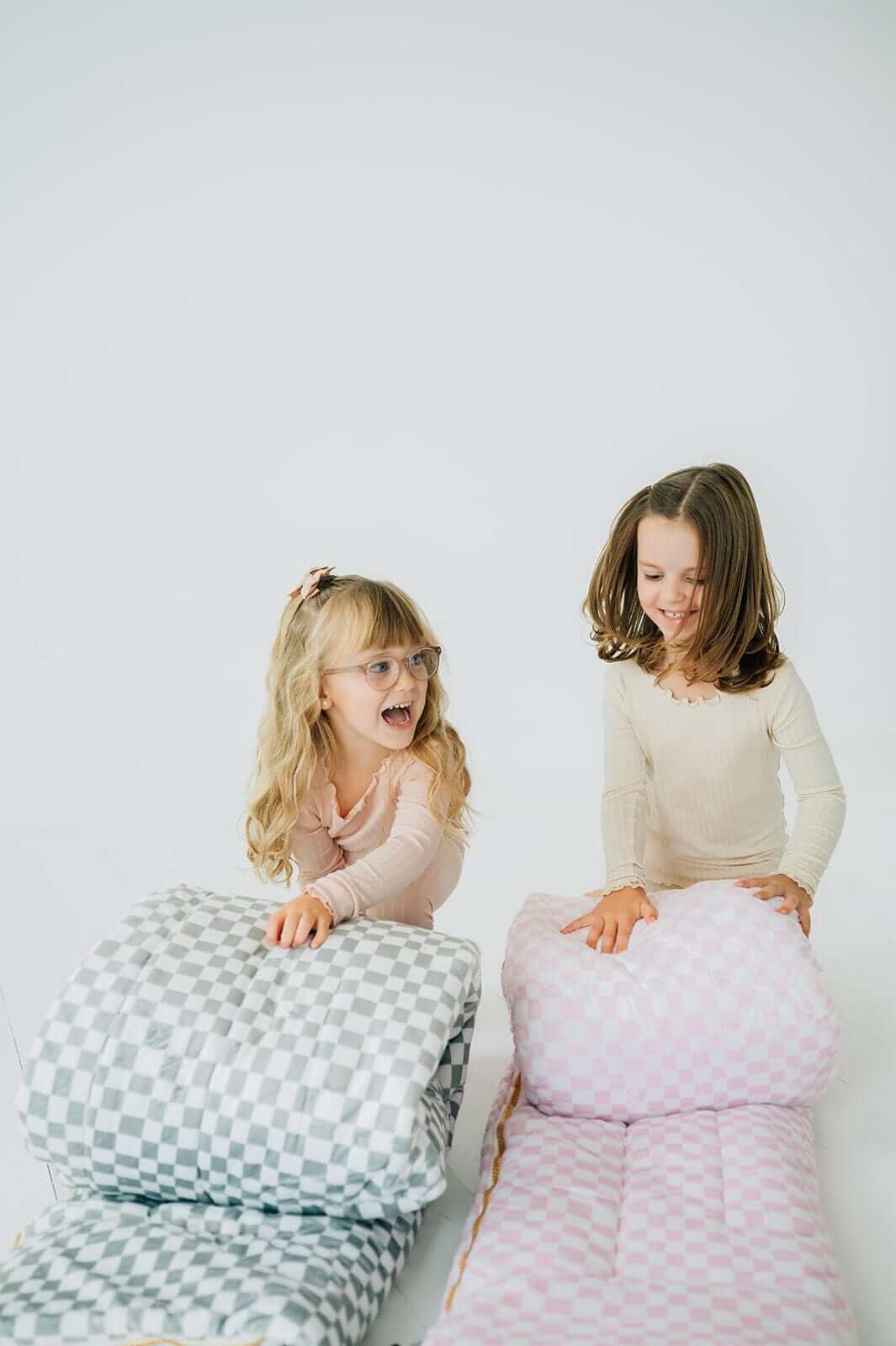 Two children playing with Sleeping Bags Pink Check and gray check patterns, showcasing comfort and fun.
