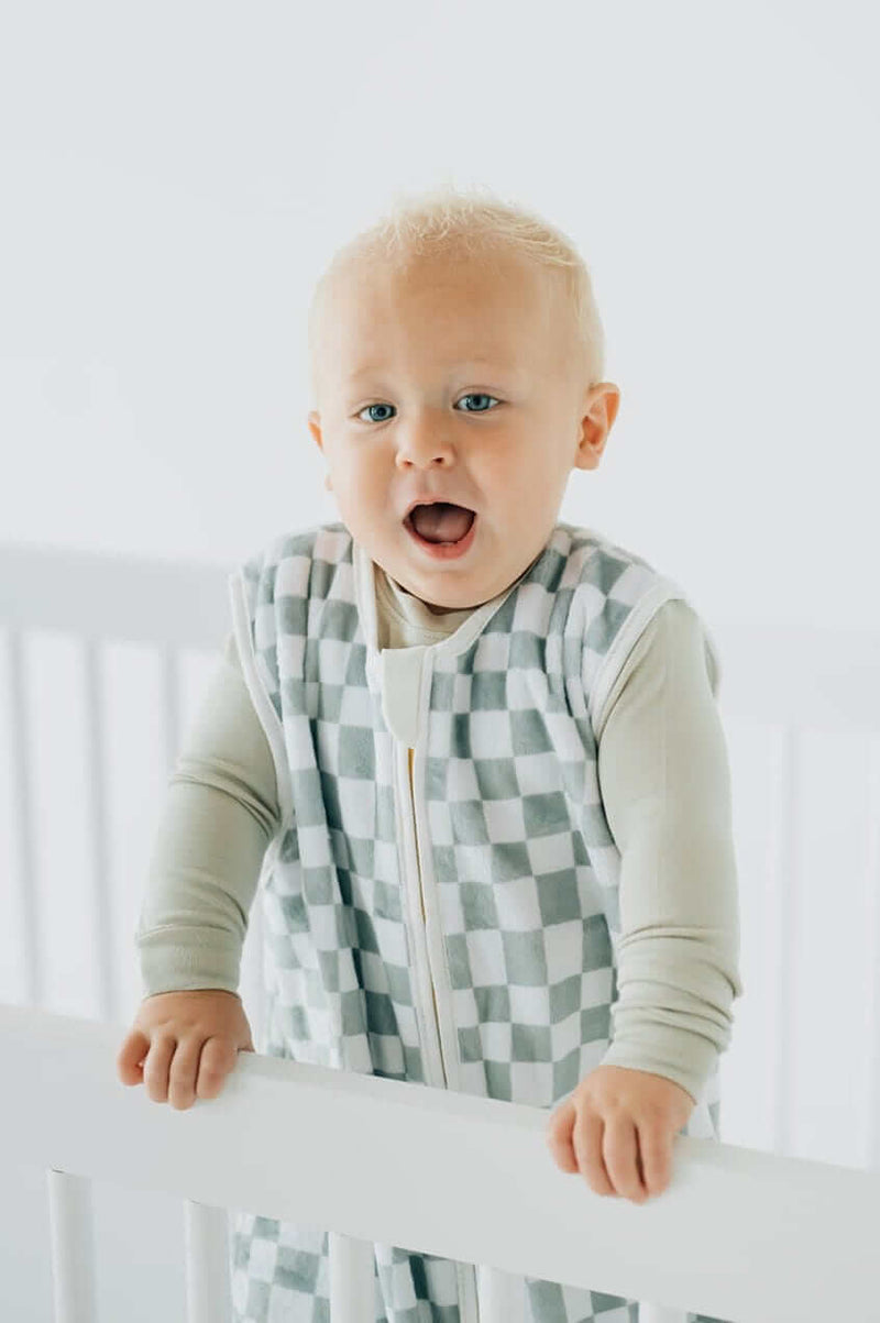 Sage Check Wearable Minky Couture Blanket on a baby standing in a crib, showcasing comfort and safety.
