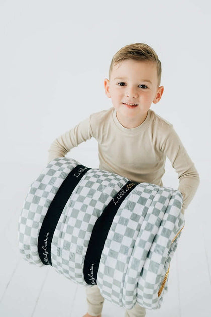Child carrying a rolled Sage Check Sleeping Bag from Little Couture by Minky Couture.