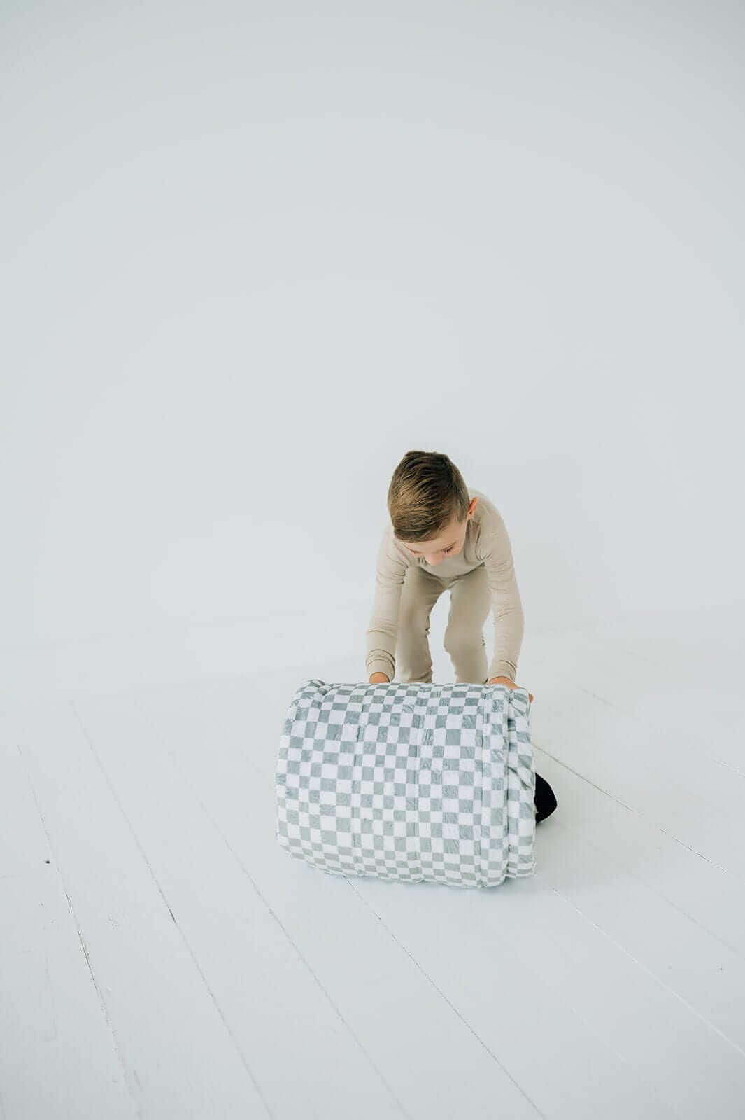 Child rolling up Sleeping Bag Sage Check for easy storage and portability, showcasing its functional design.