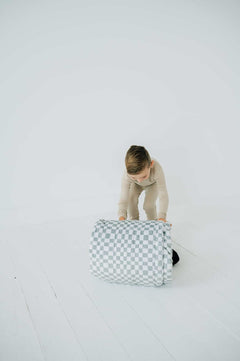 Child rolling up Sleeping Bag Sage Check for easy storage and portability, showcasing its functional design.