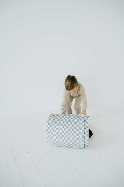 Child rolling up Sleeping Bag Sage Check for easy storage and portability, showcasing its functional design.
