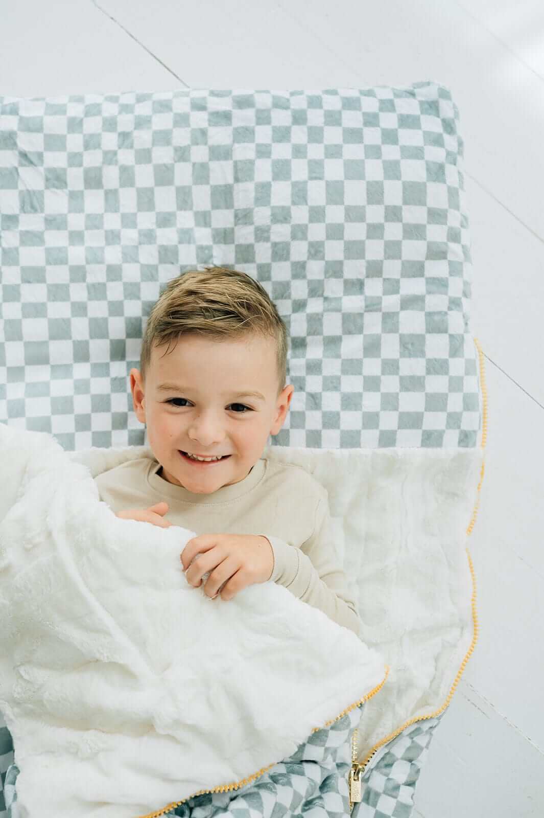 Child snuggled in a cozy Sage Check Sleeping Bag with plush lining, ready for a slumber party.