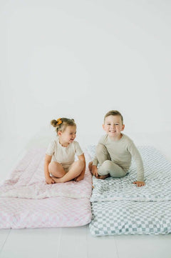 Two children sitting on colorful sleeping bags showcasing the Sleeping Bag in Sage Check design.