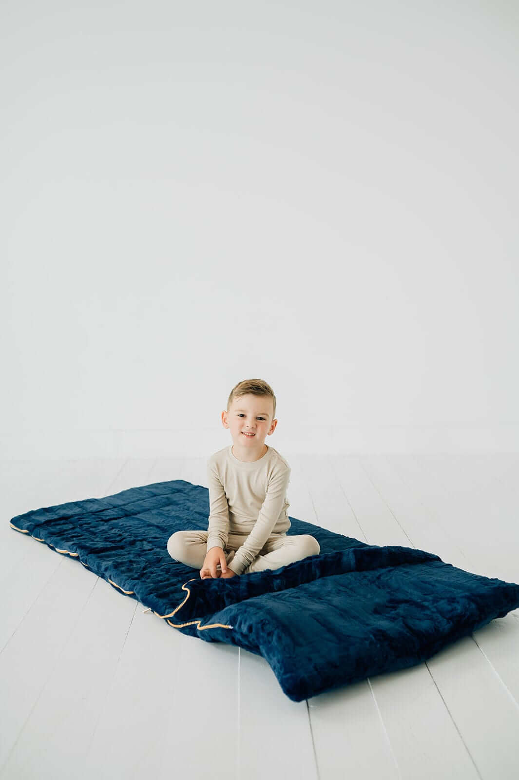 Little Couture Sleeping Bag Navy, with a child sitting on it, showing the plush design and cozy fabric.