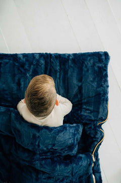 Top view of a child snuggled in a Navy Sleeping Bag, featuring a plush Minky shell and cozy lining.