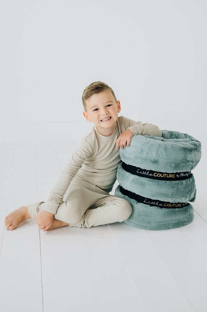 Plush Mist Sleeping Bag by Little Couture with a boy sitting next to soft plush storage pillows in a cozy setting.