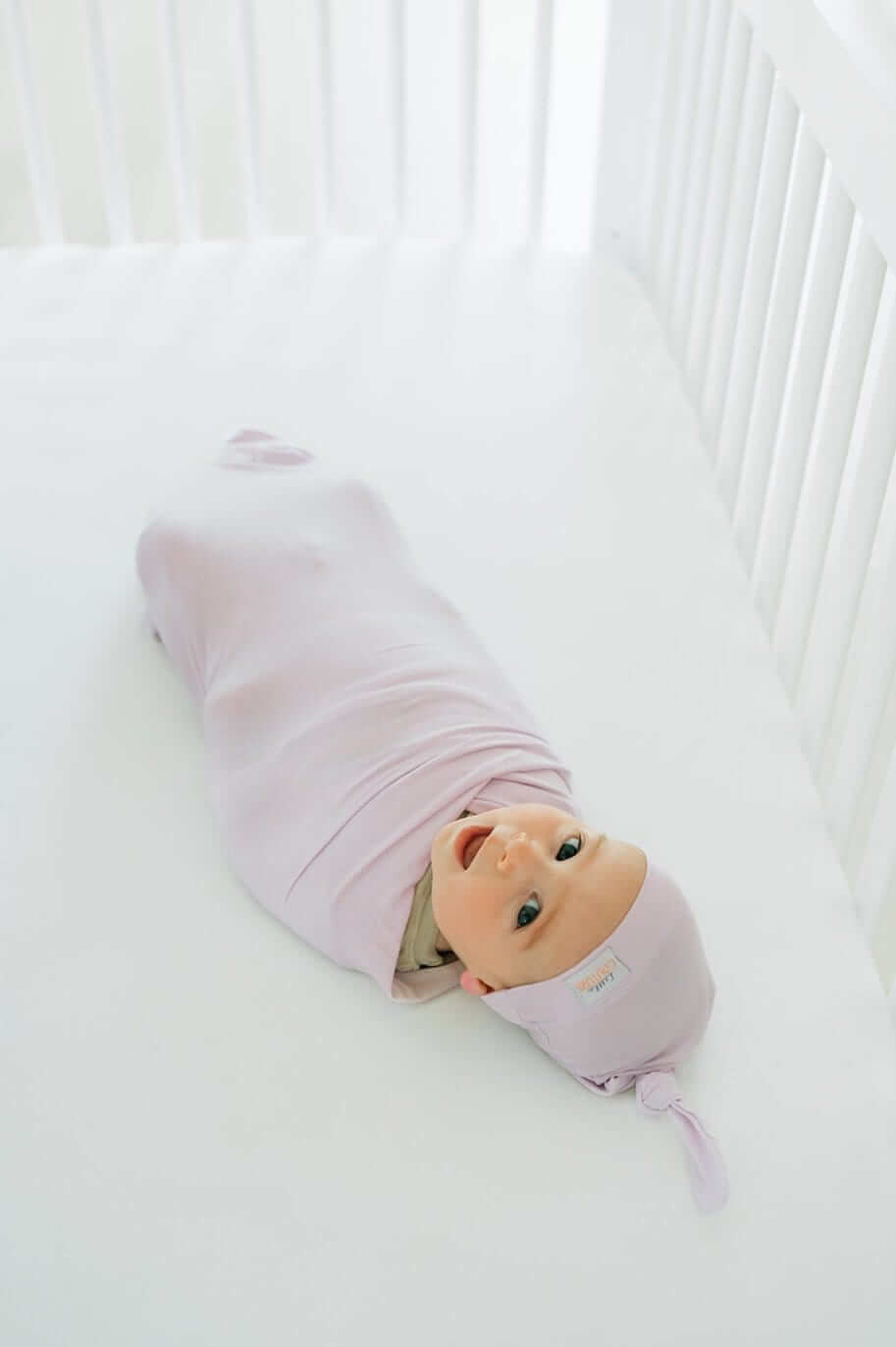 Baby bundled in soft bamboo Lavender Swaddle and Hat, cozy in crib.