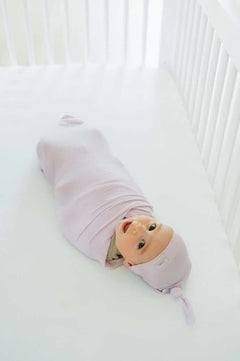 Baby bundled in soft bamboo Lavender Swaddle and Hat, cozy in crib.