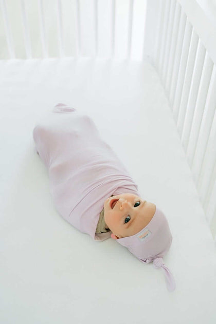 Baby bundled in soft bamboo Lavender Swaddle and Hat, cozy in crib.