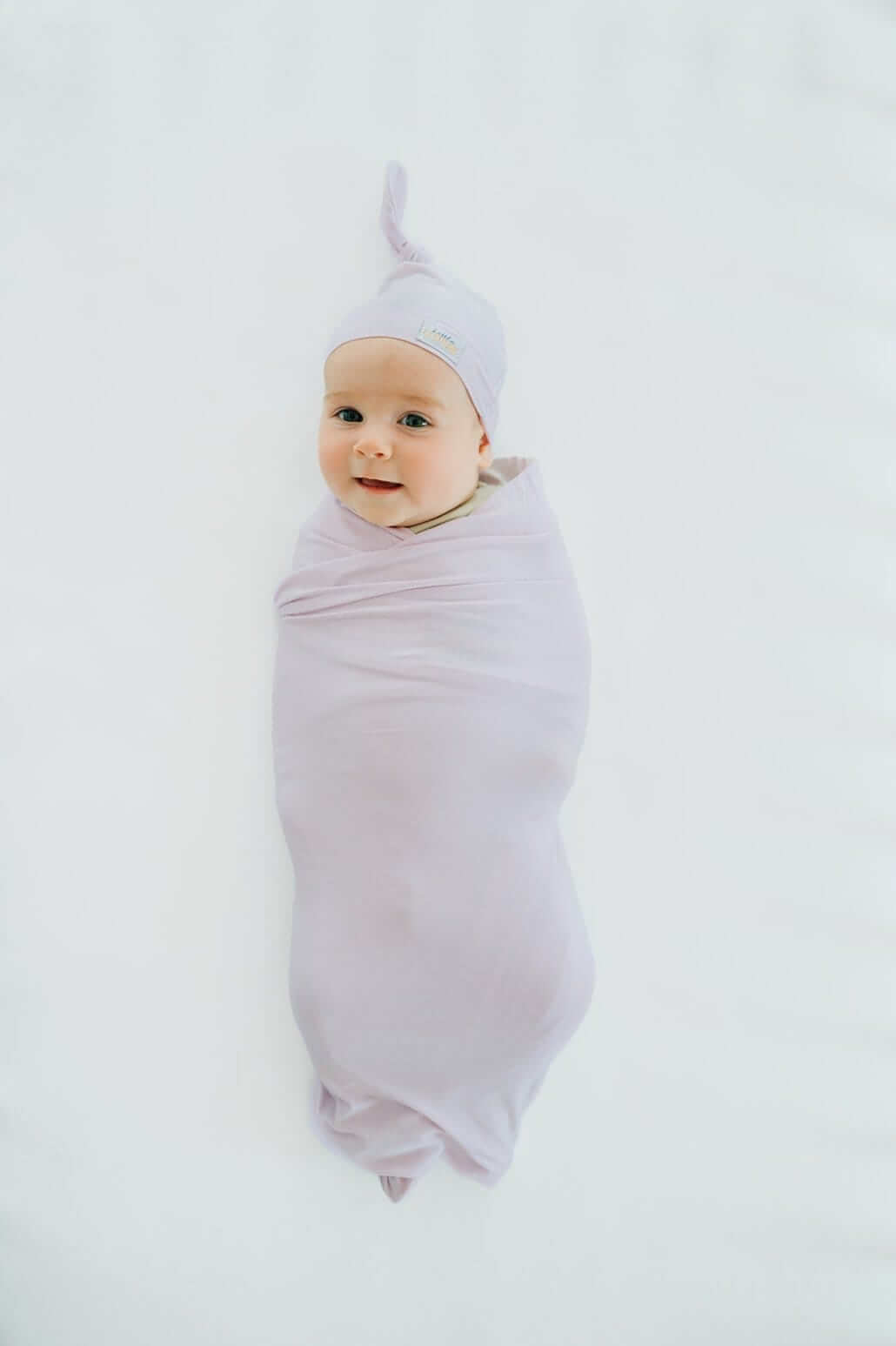 Baby bundled in soft bamboo Lavender swaddle and matching hat, looking cozy and content.