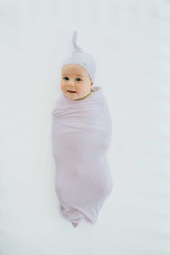 Baby bundled in soft bamboo Lavender swaddle and matching hat, looking cozy and content.