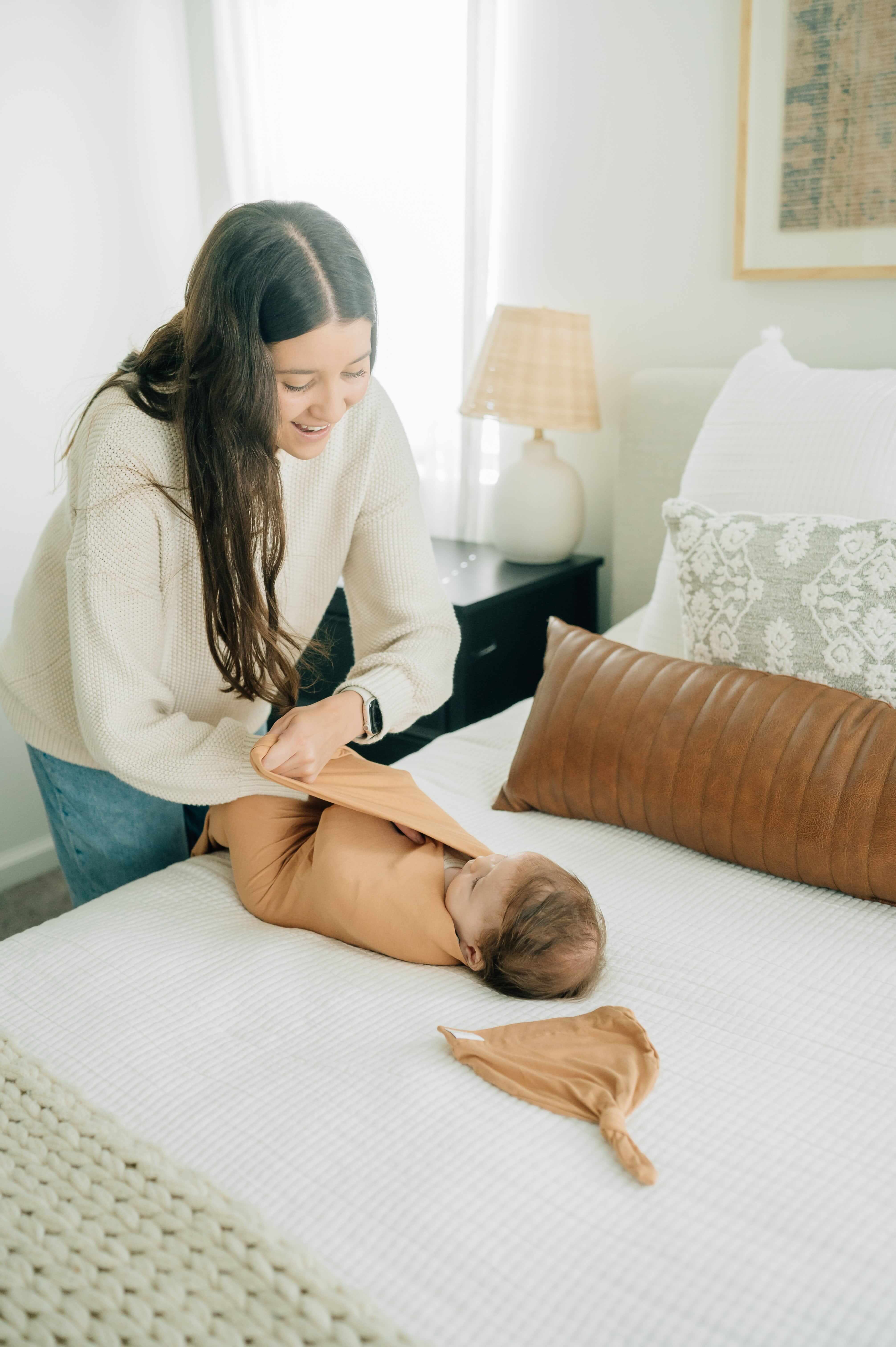 Mom wrapping her baby in a Swaddle and Hat Baked Apple Pie on a cozy bed in a stylish nursery.