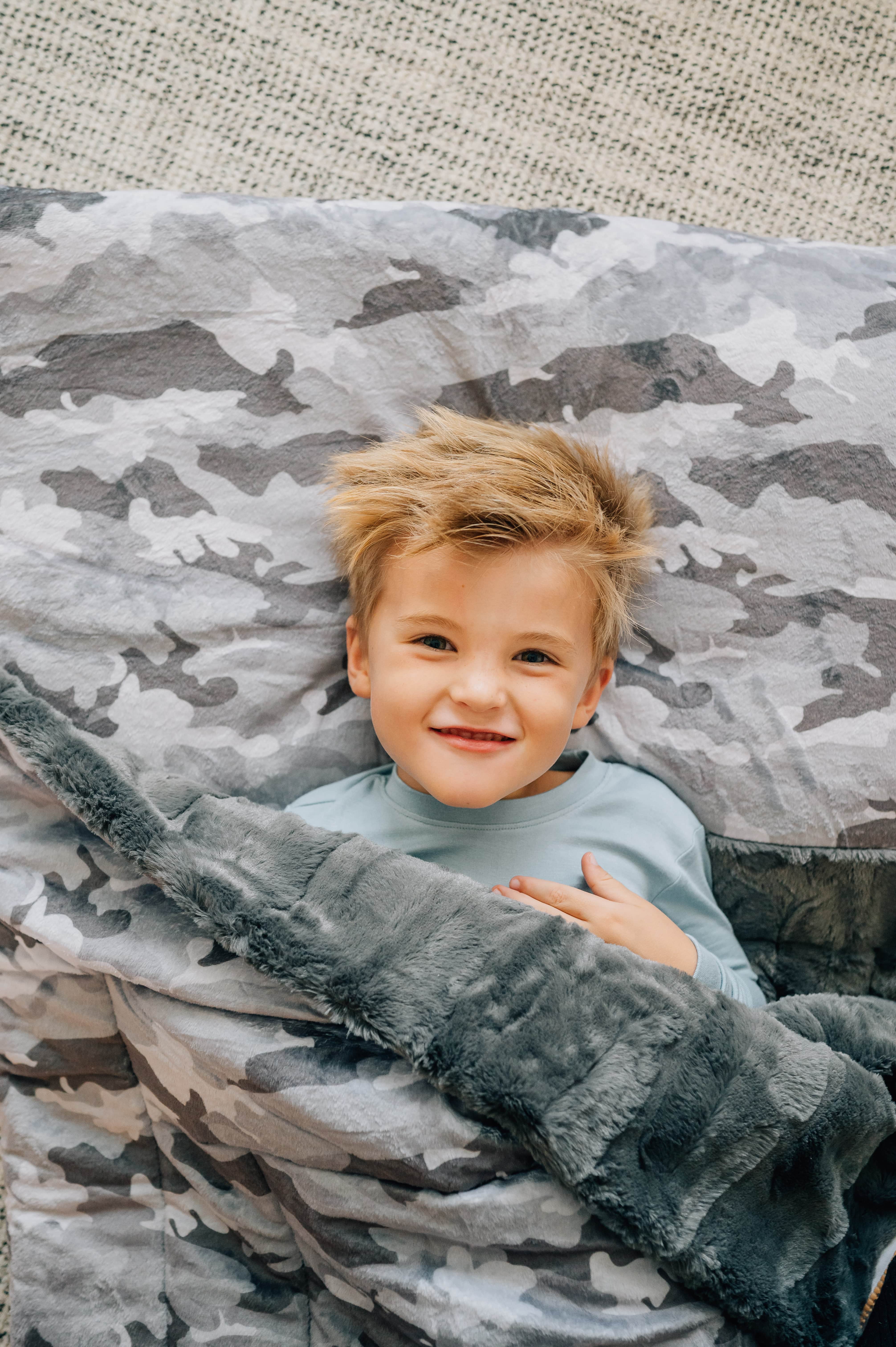 Minky Couture Camo Sleeping Bag with a happy child snug underneath on a cozy surface.