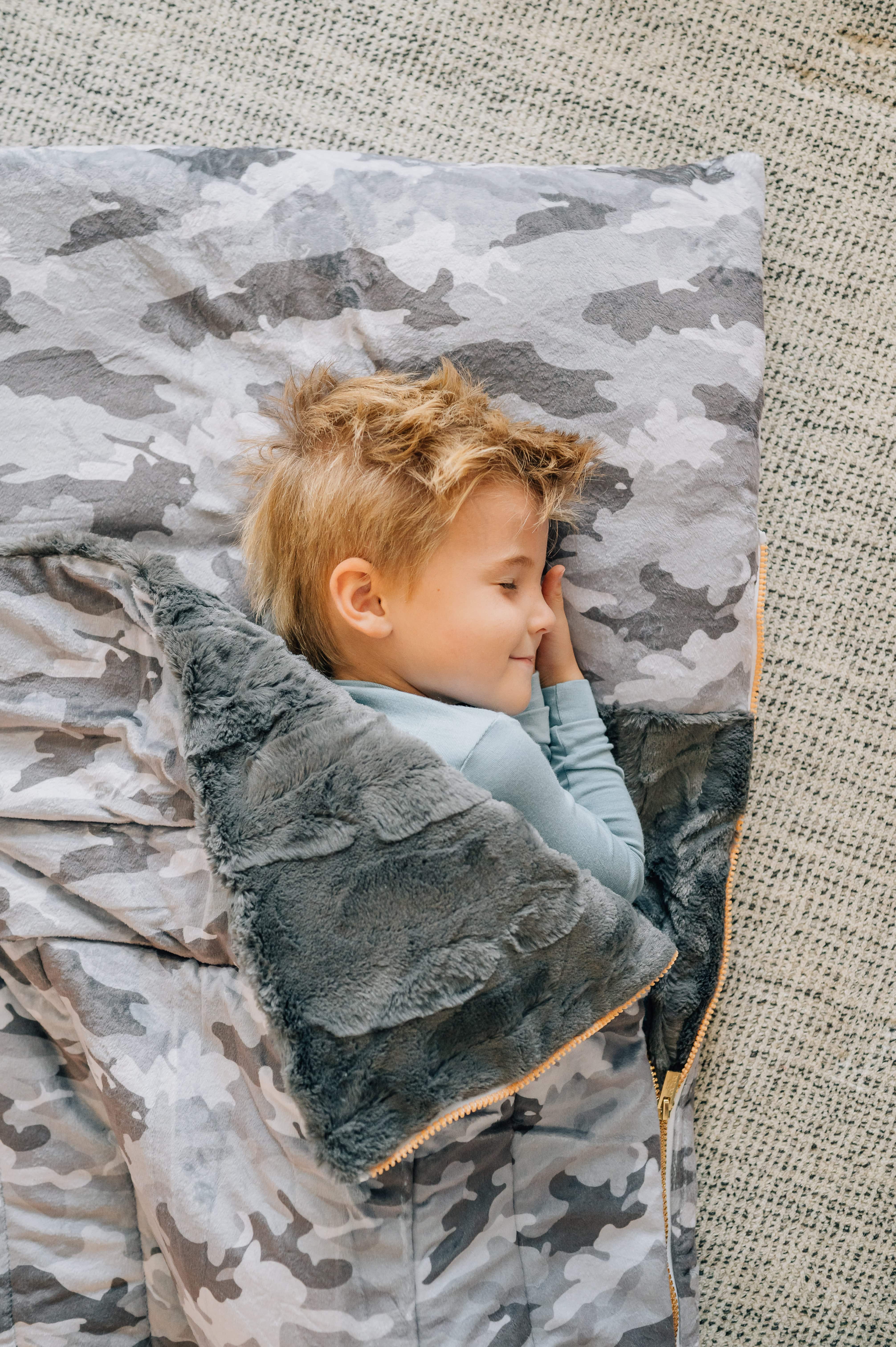 Camo Sleeping Bag with a child happily sleeping inside, featuring a plush lining and camo design.