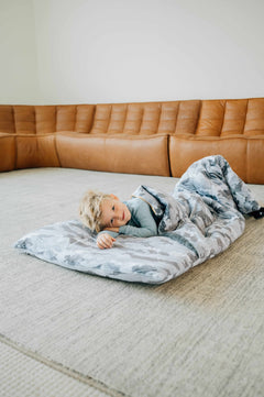 Sleeping Bag Camo featuring a child comfortably lying on a soft, plush sleeping bag in a cozy living room setting.