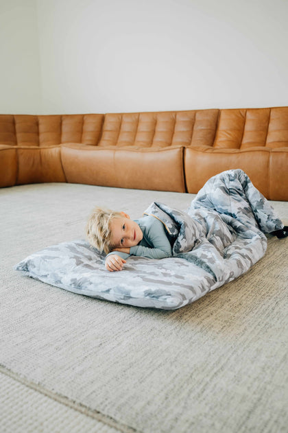 Sleeping Bag Camo featuring a child comfortably lying on a soft, plush sleeping bag in a cozy living room setting.