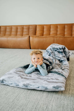 A child relaxing in a Sleeping Bag Camo on a living room floor, showcasing its plush design and comfort.