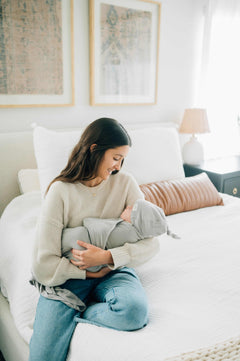 Mom cuddling her baby in a soft Swaddle and Hat Tranquil Dove on a cozy bed.