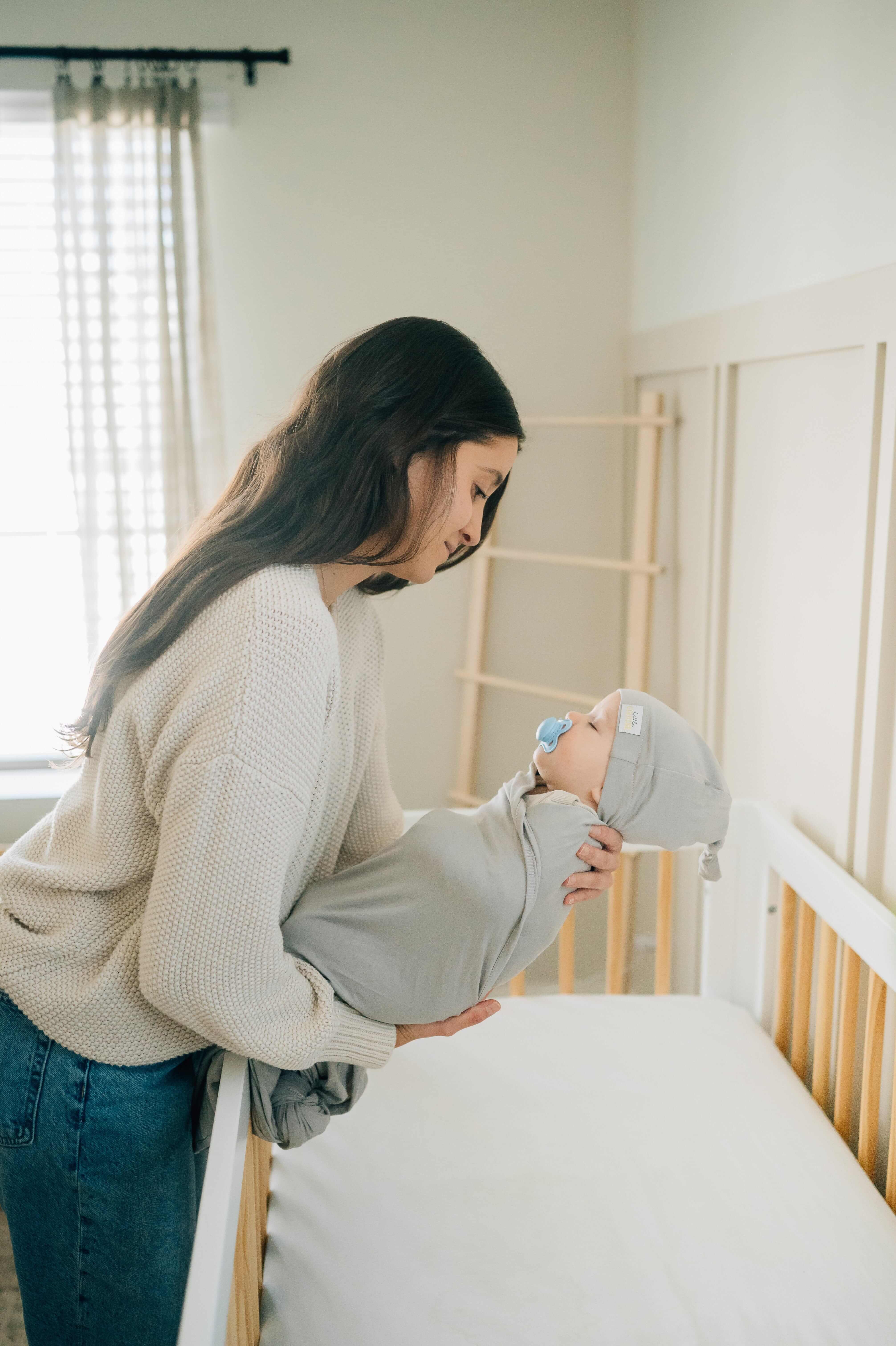 Mom cradling her baby in a Swaddle and Hat Tranquil Dove, creating a cozy sleep environment.