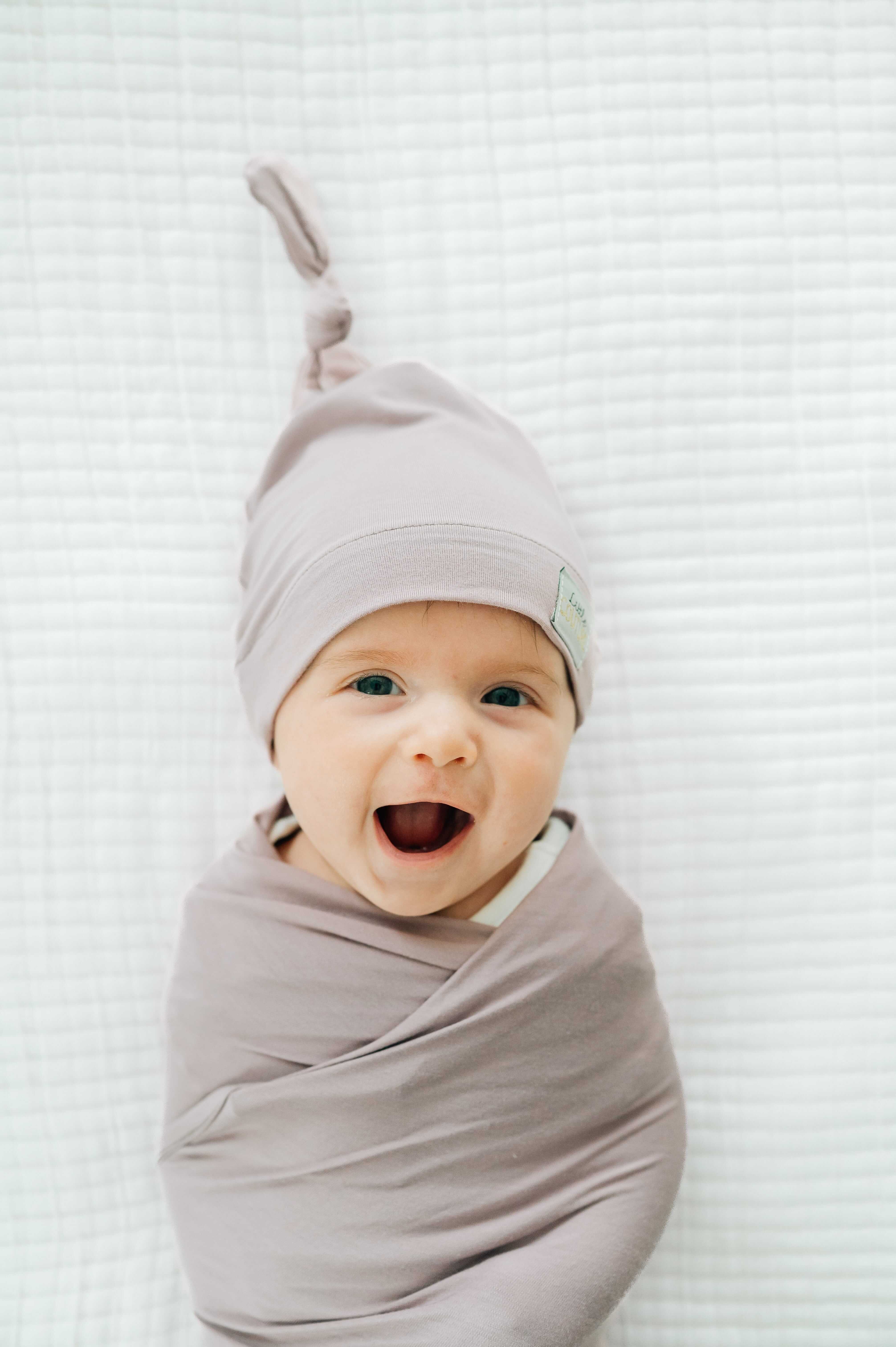 Swaddle and Hat Blueberry Cheesecake with a happy baby bundled in a cozy bamboo swaddle and matching hat.