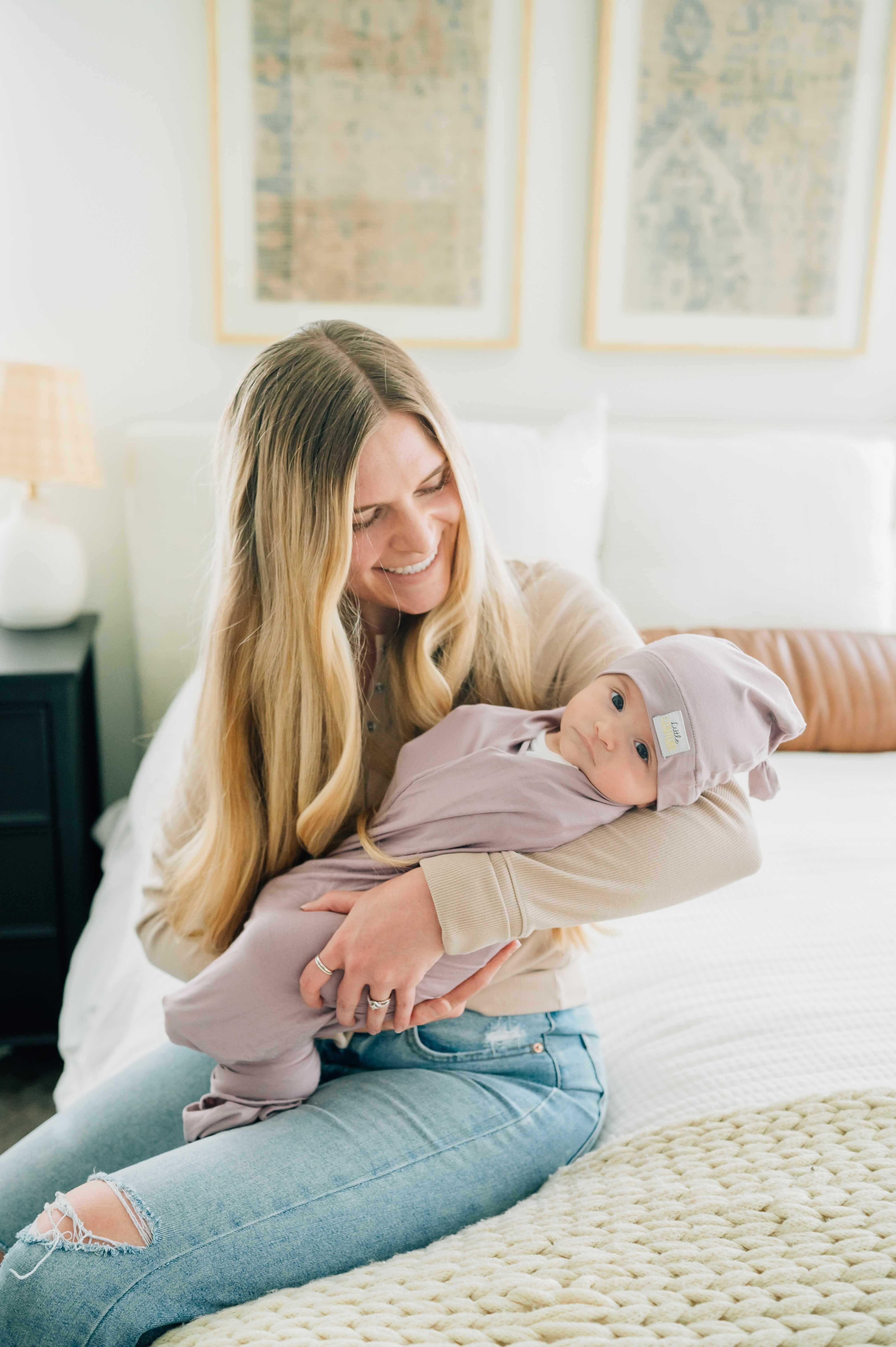 Mom cuddling baby in Swaddle and Hat Blueberry Cheesecake on a cozy bed, showcasing a stylish bonding moment.