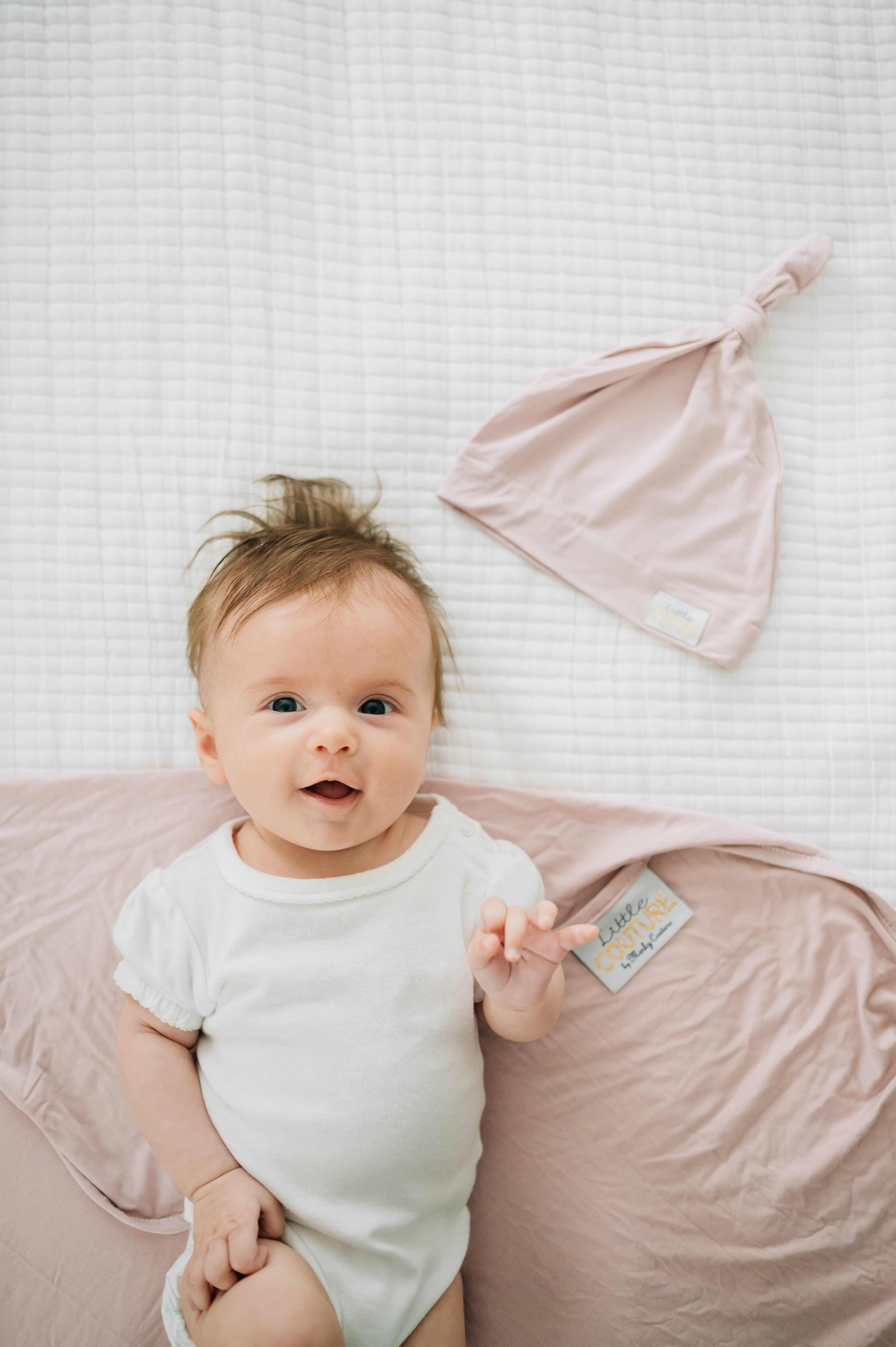 Baby wearing a onesie next to a matching bamboo hat showcasing the Swaddle and Hat Blush set.