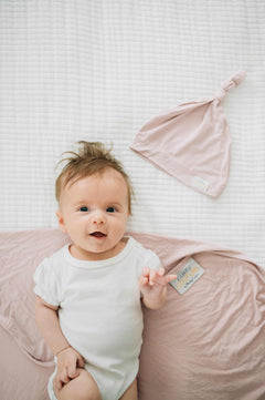 Baby wearing a onesie next to a matching bamboo hat showcasing the Swaddle and Hat Blush set.