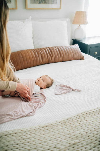 Swaddle and Hat Blush set featuring a baby swaddled and a matching hat on a cozy bed.