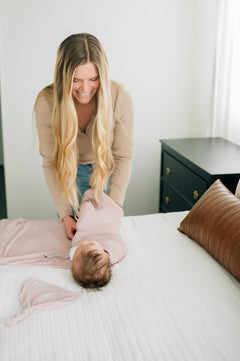 A mother gently wrapping her baby in a pink bamboo Blush Swaddle and Hat, during nap time.