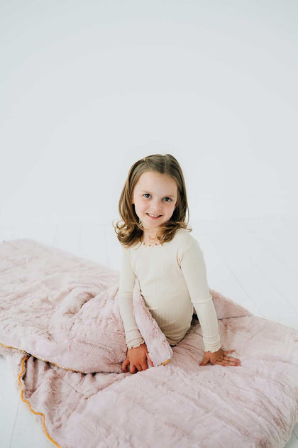 Child sitting on a  Blush Sleeping Bag, featuring soft Minky material, ideal for comfort and warmth.