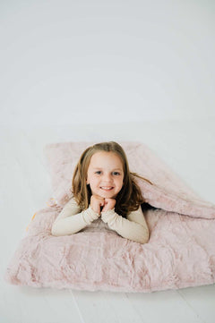 Sleeping Bag in Blush color, on a cozy surface with a child smiling and enjoying the plush fabric.