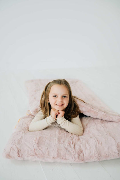 Sleeping Bag in Blush color, on a cozy surface with a child smiling and enjoying the plush fabric.