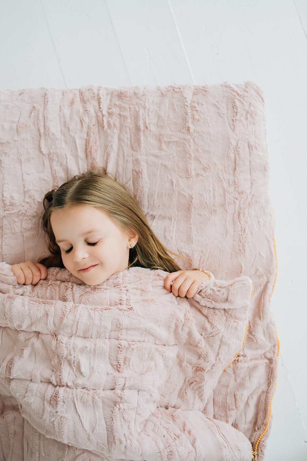 Child peacefully sleeping under a soft blush-colored sleeping bag.