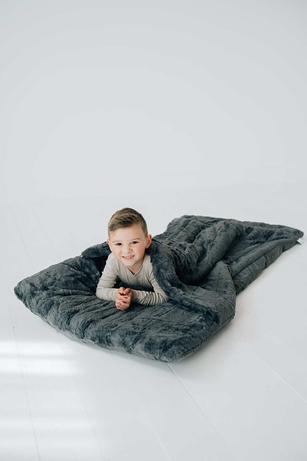 A smiling boy wrapped in a cozy Charcoal gray Sleeping Bag, perfect for comfort during sleepovers.