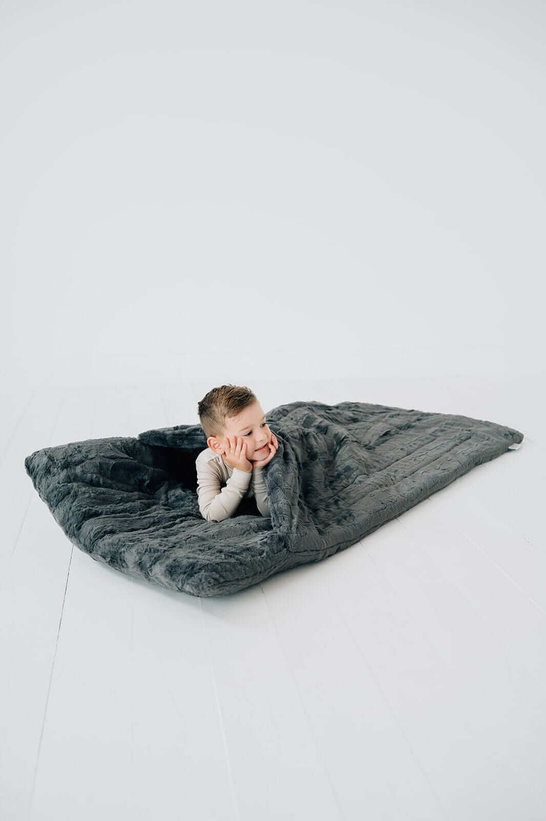 A child relaxing in a plush Charcoal Sleeping Bag, showcasing its cozy design and soft texture.