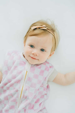 Baby in Pink Check Wearable Minky Blanket with a gold zipper, looking up with a cute headband.