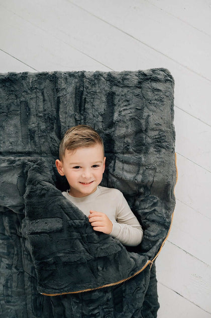 A child smiling while snuggled in a Sleeping Bag in Charcoal, with plush texture, perfect for cozy moments.
