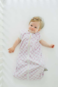 Pink Check Wearable Minky Blanket on a baby lying in a crib, showcasing its light pink check pattern and gold zipper.