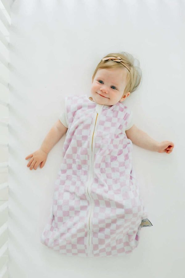 Pink Check Wearable Minky Blanket on a baby lying in a crib, showcasing its light pink check pattern and gold zipper.