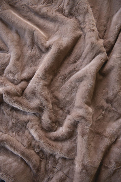A close-up of a plush, soft faux fur or sherpa blanket in a warm taupe-brown color, shown with soft folds and ripples.