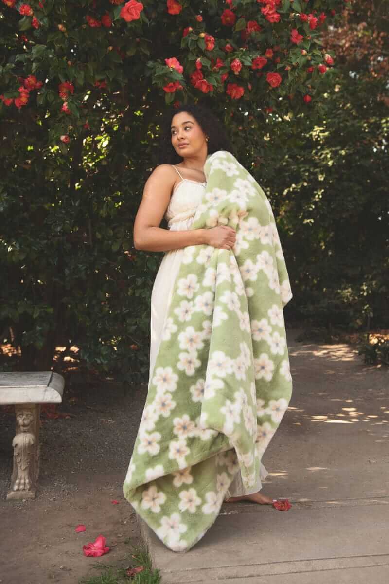 Lush Mist Floral Blanket draped over a model standing amidst blooming flowers in a garden.