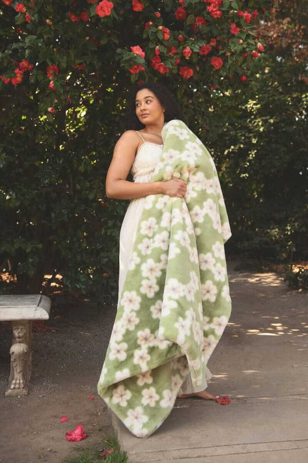 Lush Mist Floral Blanket draped over a model standing amidst blooming flowers in a garden.