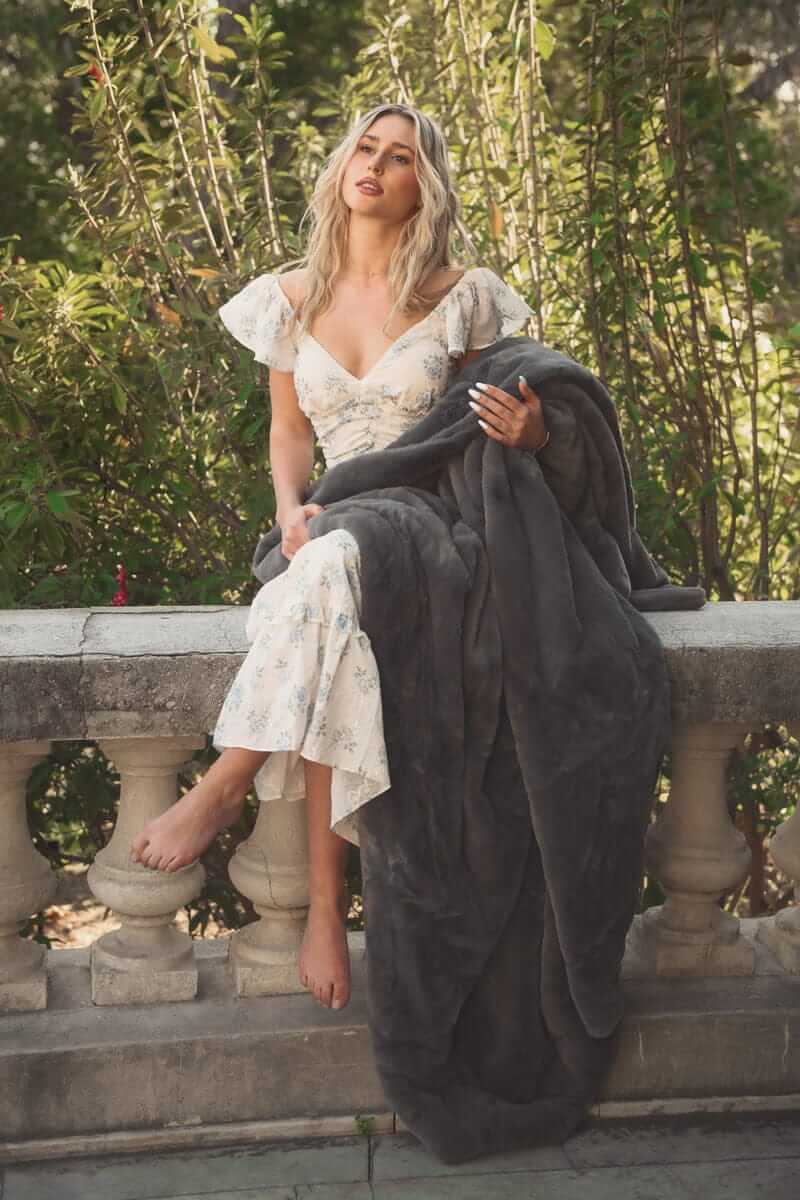 A woman relaxing outdoors, draped in the Lush Steel Gray Blanket, showcasing its elegant design and luxurious comfort.