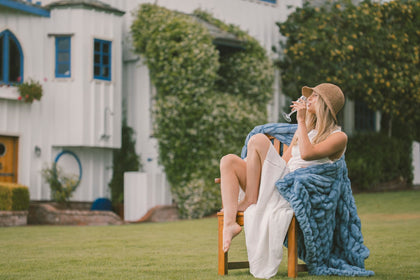Woman sitting on a chair with a blue Minky Couture Hugs blanket in a garden setting