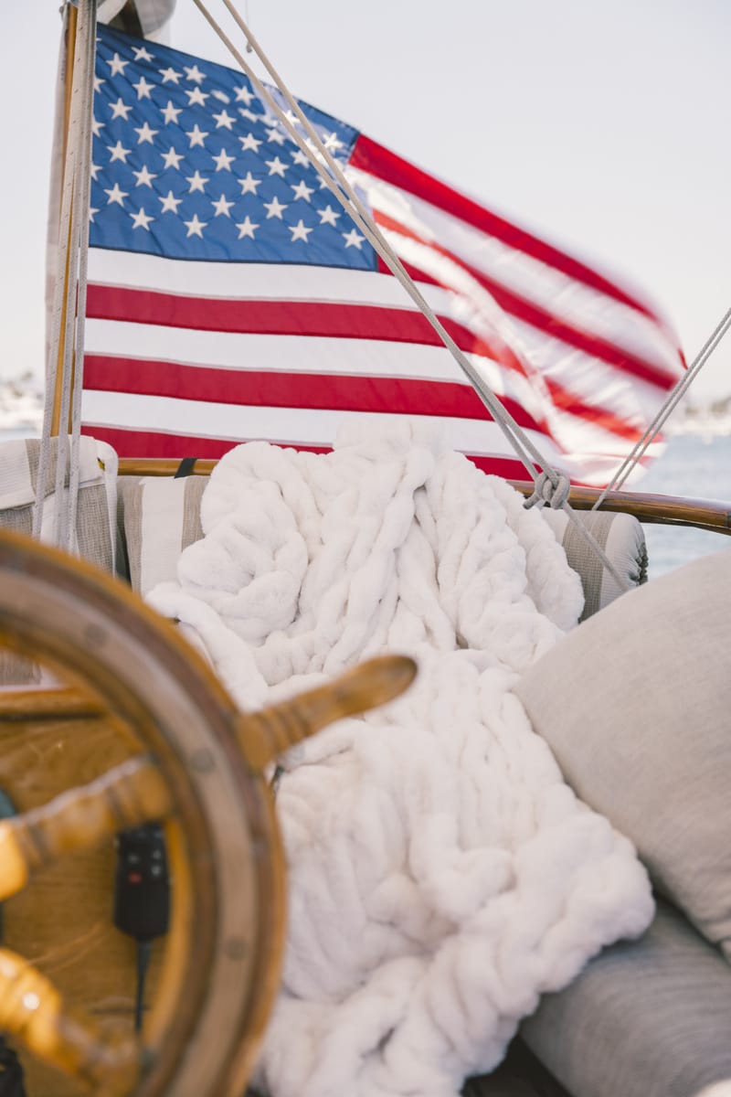 American flag on a boat with a cream Minky Couture Hugs blanket and wooden wheel in the foreground