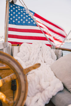 American flag on a boat with a cream Minky Couture Hugs blanket and wooden wheel in the foreground