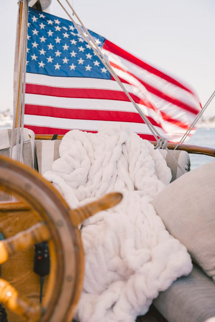 American flag on a boat with a cream Minky Couture Hugs blanket and wooden wheel in the foreground