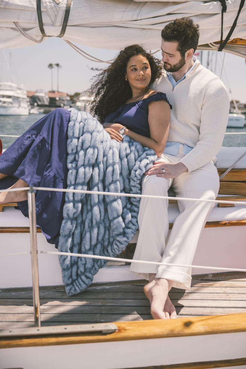 Couple sitting on a boat with a blue Hugs Minky Couture blanket, surrounded by water and boats.