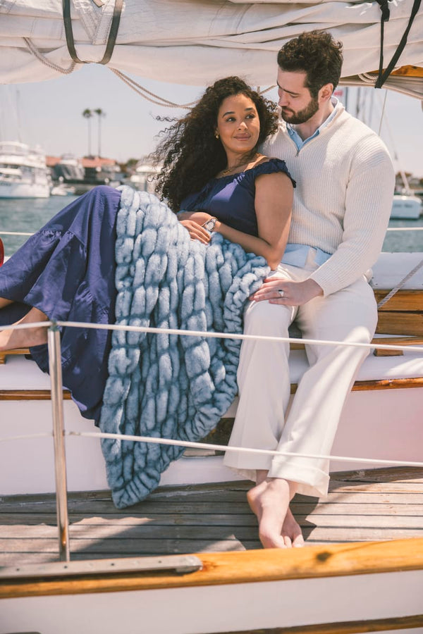 Couple sitting on a boat with a blue Hugs Minky Couture blanket, surrounded by water and boats.